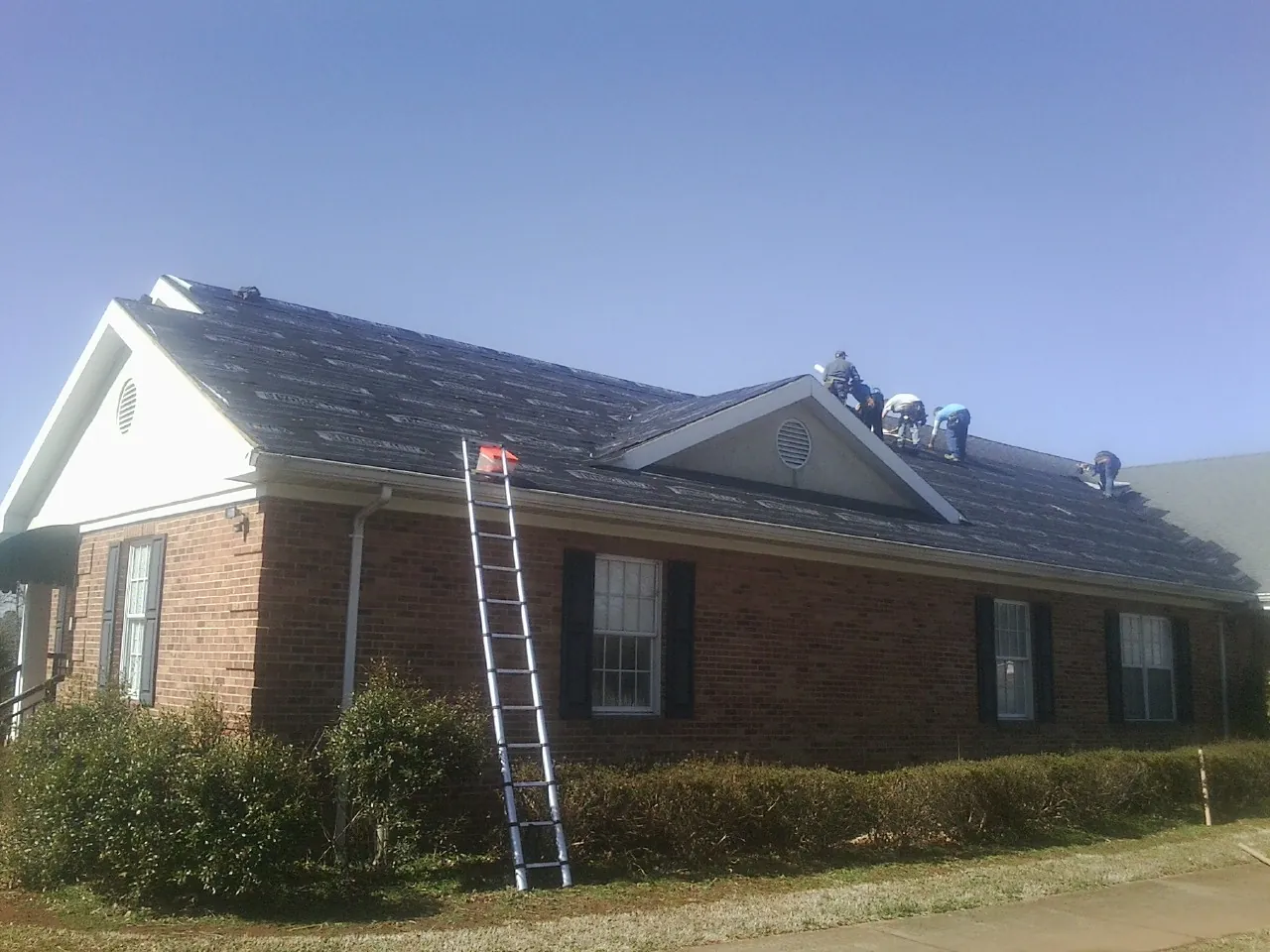 Crew tearing shingles off a brick ranch roof with a ladder set — Emergency Roof Repair work by our crew in Dayton